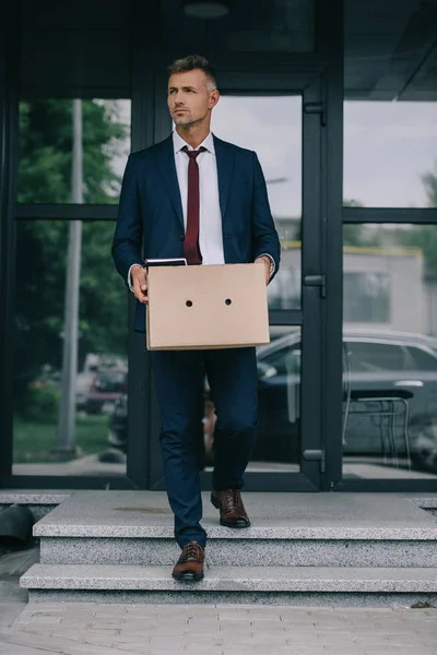 Dismissed businessman walking on stairs near building and holding box — Stock Photo