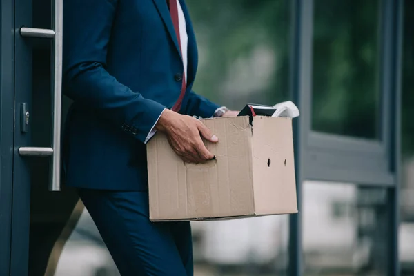 Cropped view of fired businessman standing near building and holding carton box — Stock Photo