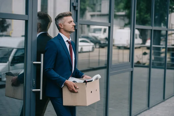 Звільнений чоловік у костюмі, що стоїть біля будівлі з картонною коробкою — стокове фото