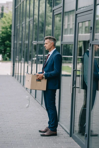 Vista lateral do homem demitido em terno de pé perto do edifício com telefone retro na caixa de papelão — Fotografia de Stock