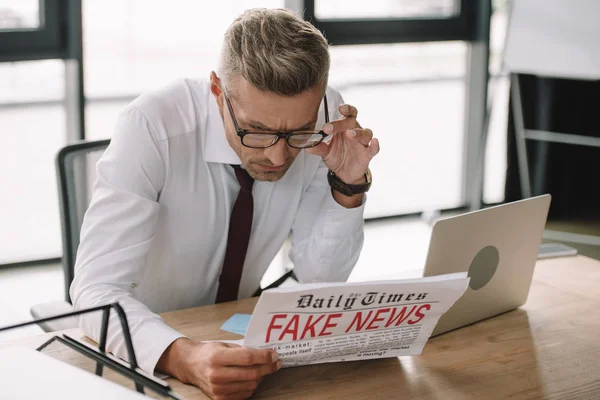 Вибірковий фокус бізнесмена торкаючись окулярів під час читання газети з фальшивими новинами — стокове фото