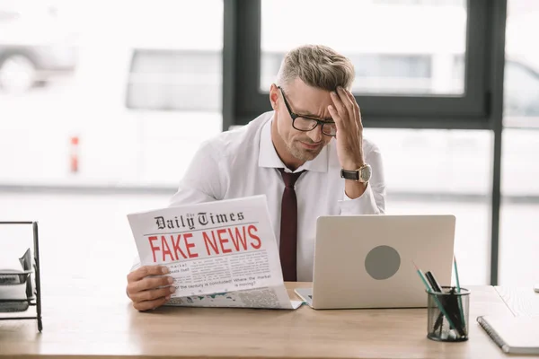 Upset businessman in glasses holding newspaper with fake news — Stock Photo