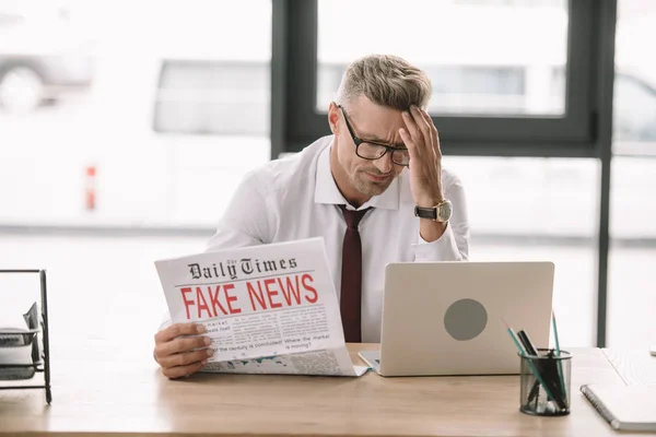 Bouleversé homme d'affaires dans des lunettes tenant journal avec de fausses nouvelles — Photo de stock