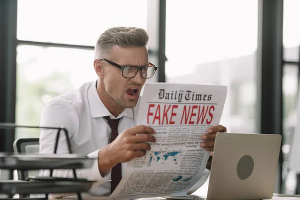 Sorprendido hombre de negocios en gafas de leer el periódico con noticias falsas - foto de stock