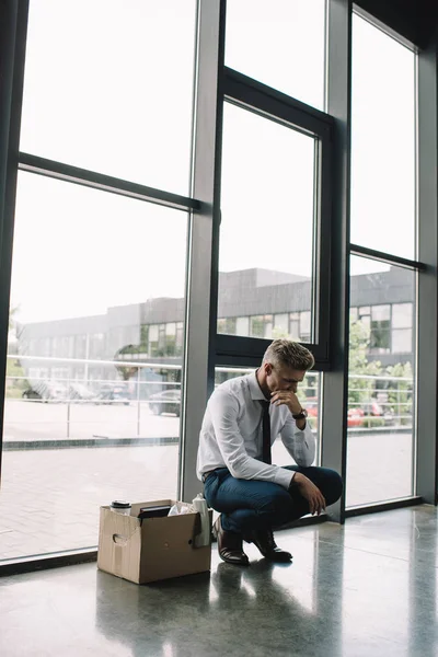 Demitido empresário cobrindo boca enquanto sentado caixa de papelão no escritório — Fotografia de Stock
