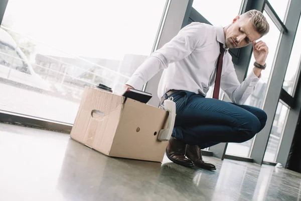 Засмучений бізнесмен дивиться на картонну коробку в офісі — стокове фото