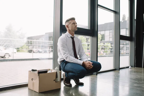 Bouleversé et viré homme en costume assis près de la boîte en carton — Photo de stock