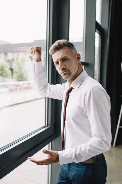 Displeased businessman in suit standing near windows with clenched fist — Stock Photo