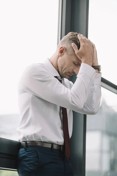 Triste hombre de negocios tocando el pelo mientras está de pie cerca de ventanas - foto de stock