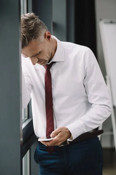 Verärgerter Geschäftsmann steht im Anzug und nutzt Smartphone — Stockfoto