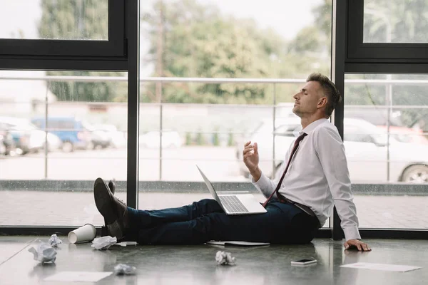 Seitenansicht eines gutaussehenden Geschäftsmannes mit geschlossenen Augen, der mit Laptop auf dem Boden sitzt — Stockfoto