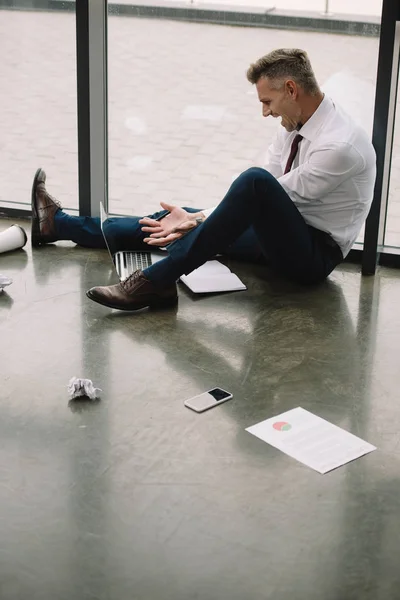 Unzufriedener Mann gestikuliert, während er auf dem Boden sitzt und auf Laptop schaut — Stockfoto