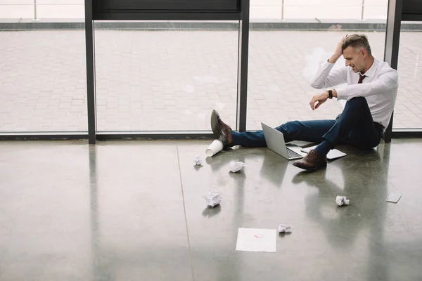 Вид збоку незадоволений чоловік сидить на підлозі і дивиться на ноутбук — стокове фото