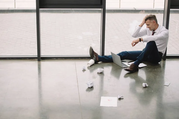 Side view of displeased man sitting on floor and looking at laptop — Stock Photo