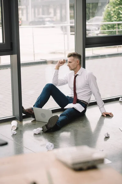 Enfoque selectivo de hombre de negocios sentado en el piso cerca de las ventanas - foto de stock
