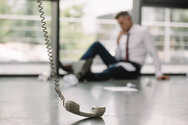 Selective focus of retro phone near businessman sitting on floor near windows — Stock Photo