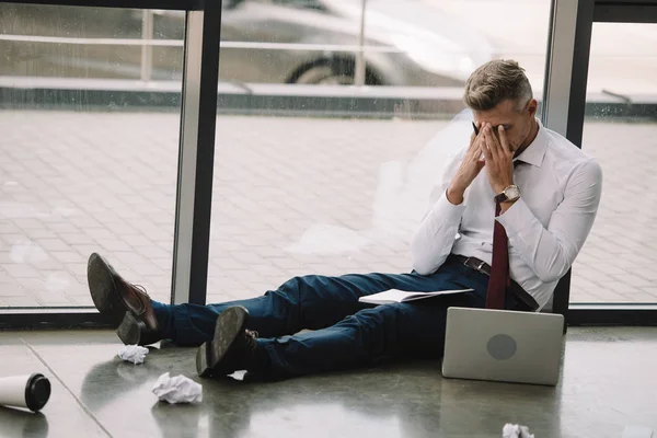 Aufgebrachter Geschäftsmann sitzt auf dem Boden und bedeckt Gesicht mit Händen in der Nähe von Laptop — Stockfoto