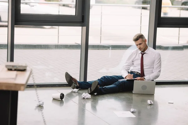 Selective focus of businessman writing in notebook near laptop — Stock Photo