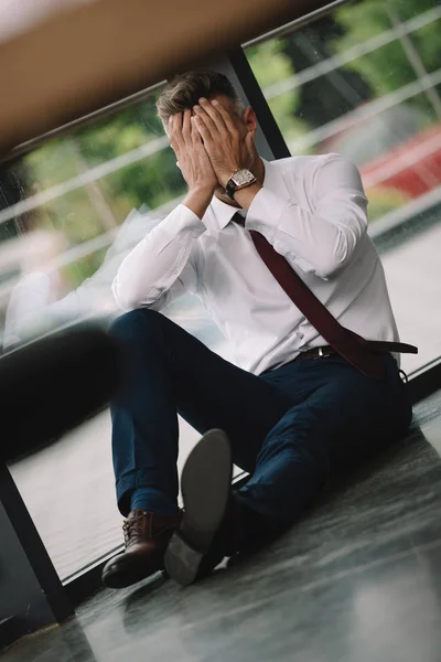 Селективный фокус грустного мужчины, закрывающего лицо руками, сидя на полу — стоковое фото