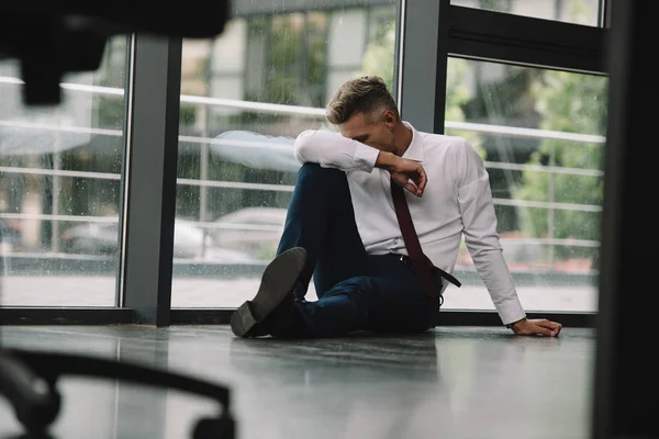 Selektiver Fokus des Mannes, der das Gesicht verdeckt, während er auf dem Boden in der Nähe von Fenstern sitzt — Stockfoto