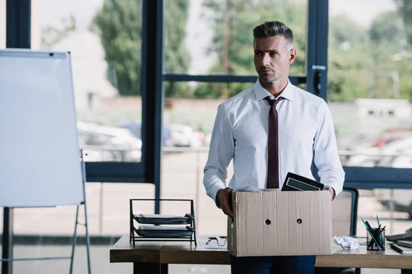 Selektiver Fokus eines gutaussehenden Geschäftsmannes mit Box in der Nähe seines Arbeitsplatzes — Stockfoto