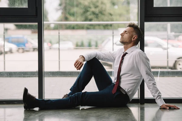Красивый бизнесмен в формальной одежде сидит на полу возле окон — стоковое фото