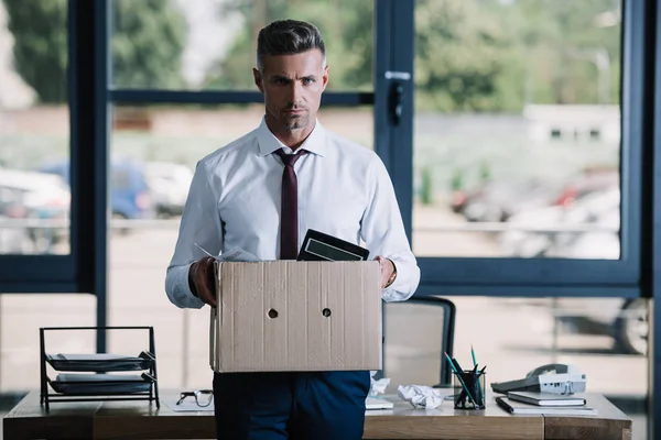Serious businessman holding box while looking at camera — Stock Photo