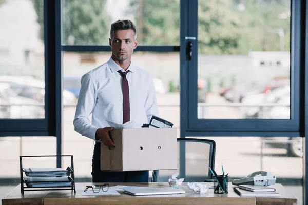 Dismissed businessman holding box while standing near workplace — Stock Photo