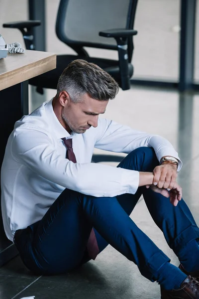 Upset businessman sitting on floor near workplace in office — Stock Photo