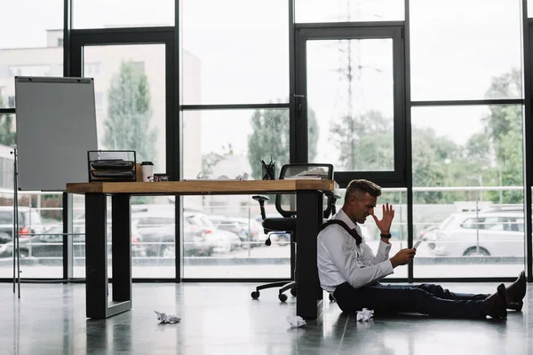 Chateado homem de negócios sentado no chão perto da mesa no escritório moderno — Fotografia de Stock