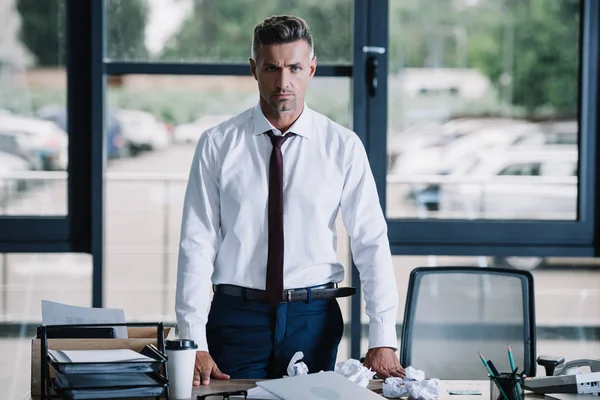 Seriöser Geschäftsmann blickt in die Kamera in der Nähe von Schreibtisch im Büro — Stockfoto