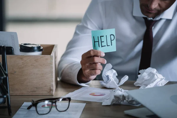 Cropped view of upset businessman holding sticky note with help lettering near table — Stock Photo