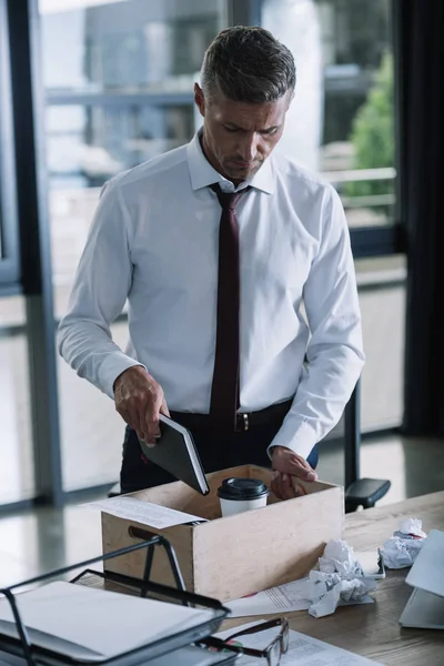 Hombre despedido poner cuaderno en caja de madera cerca de la taza de papel y bolas de papel arrugado en la mesa - foto de stock