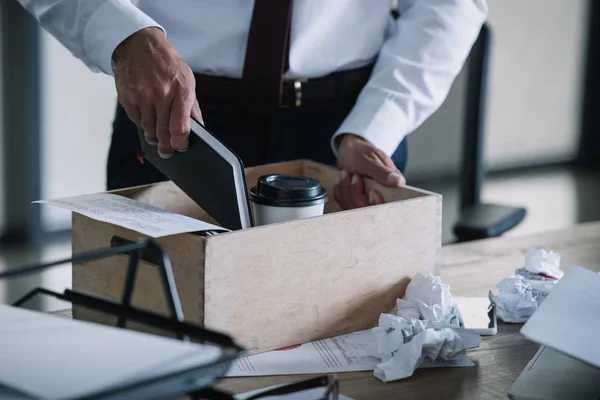 Cropped view of man putting notebook in wooden box near paper cup and crumpled paper balls on table — Stock Photo