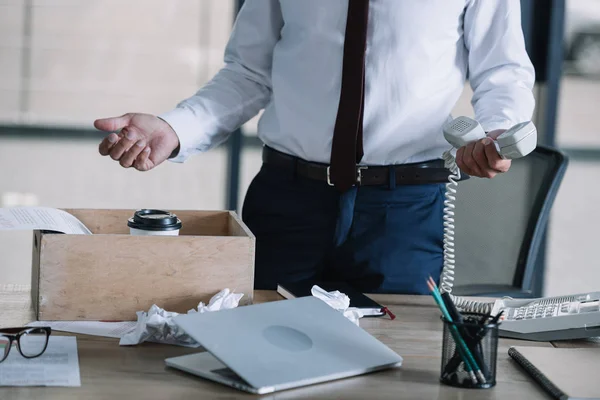 Vista cortada do homem segurando telefone retro perto de caixa de madeira e bolas de papel amassadas na mesa — Stock Photo