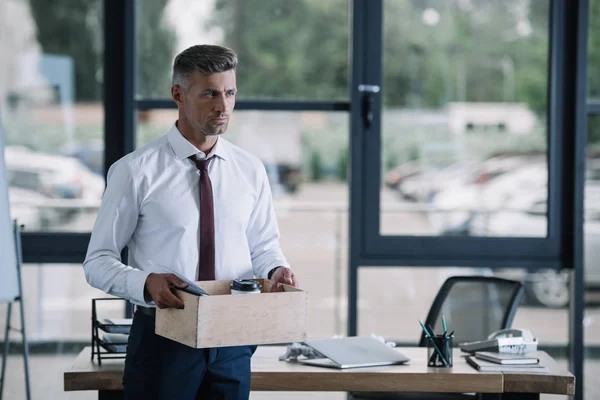 Homme d'affaires sérieux tenant la boîte tandis que debout dans le bureau — Photo de stock