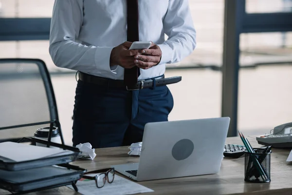 Vista ritagliata di uomo d'affari utilizzando smartphone vicino laptop in ufficio — Foto stock