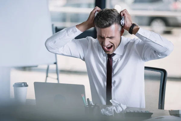 Enfoque selectivo del hombre enojado mirando a la computadora portátil en la oficina - foto de stock