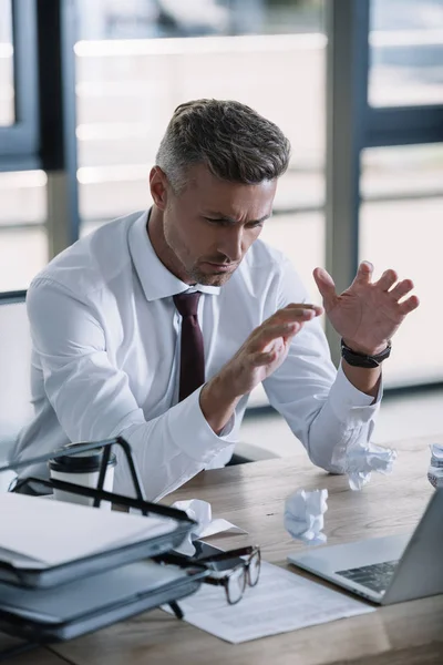 Foyer sélectif de l'homme bouleversé gesticulant près d'un ordinateur portable au bureau — Photo de stock