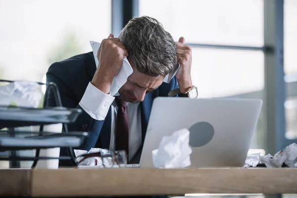 Selective focus of upset man in suit holding crumpled paper near laptop — Stock Photo