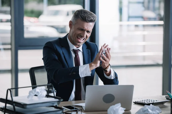 Enfoque selectivo de hombre de negocios enojado sosteniendo papel arrugado cerca de la computadora portátil en la oficina - foto de stock