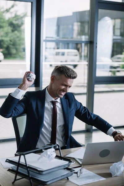 Selective focus of angry businessman holding crumpled paper in office — Stock Photo