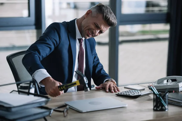 Selective focus of angry businessman holding hammer near laptop in office — Stock Photo