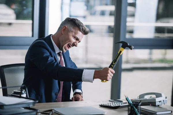 Selective focus of angry businessman holding hammer near phone on table — Stock Photo