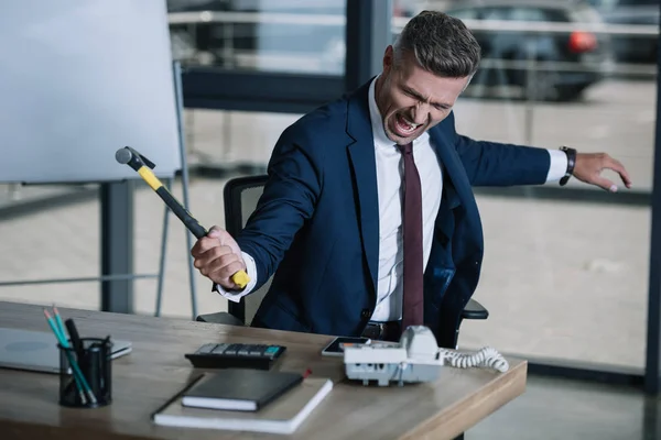 Selective focus of angry businessman holding hammer near table — Stock Photo