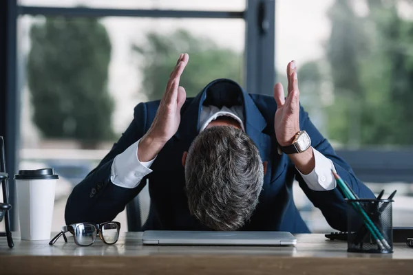 Uomo d'affari gesticolando vicino alla scrivania con tazza di carta in ufficio moderno — Foto stock