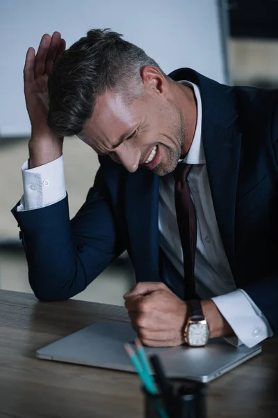 Selektiver Fokus eines wütenden Mannes, der neben Laptop im Büro sitzt — Stockfoto