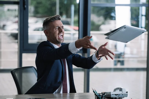 Angry businessman throwing in air laptop in office — Stock Photo