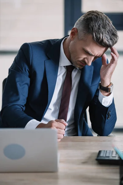 Enfoque selectivo de empresario triste en el desgaste formal cerca de la computadora portátil en la oficina - foto de stock