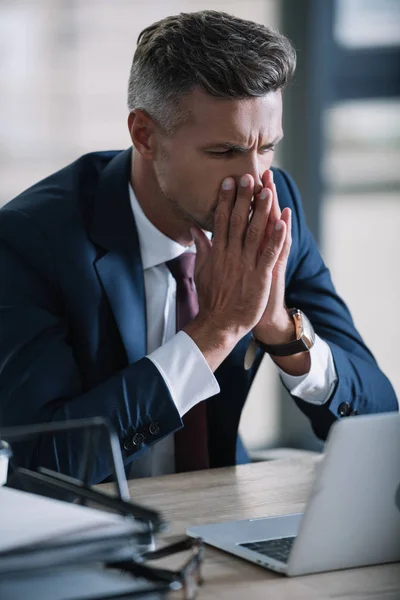 Избирательный фокус грустного бизнесмена в формальной одежде глядя на ноутбук в офисе — стоковое фото